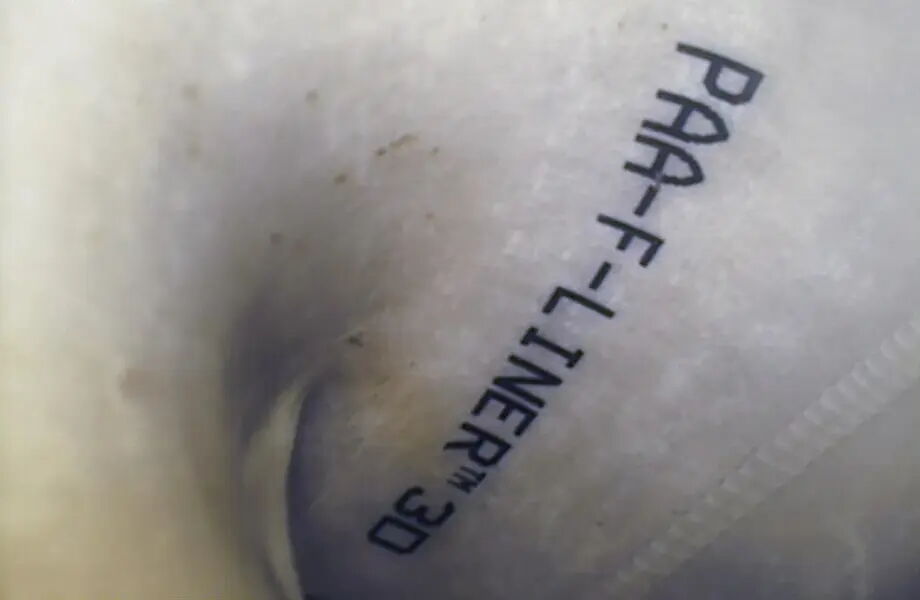 Ein nah aufgenommenes Bild eines weißen, stoffartigen Materials mit schwarzem, vertikalem Text "PAA-F-LINER TM 3D". Die Oberfläche hat leichte Falten und eine Naht ist erkennbar.