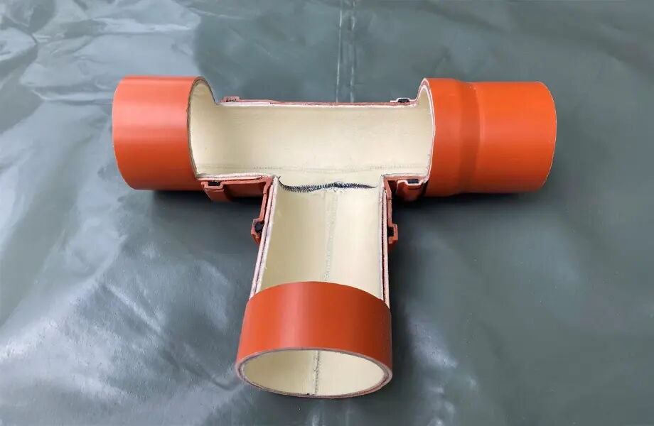 Das Bild zeigt ein T-Stück Rohr mit einer Schnittdarstellung. Die Außenseite ist orange, die Innenseite hell. Es liegt auf einer grauen Oberfläche und zeigt die Verbindung der Röhren im Inneren.