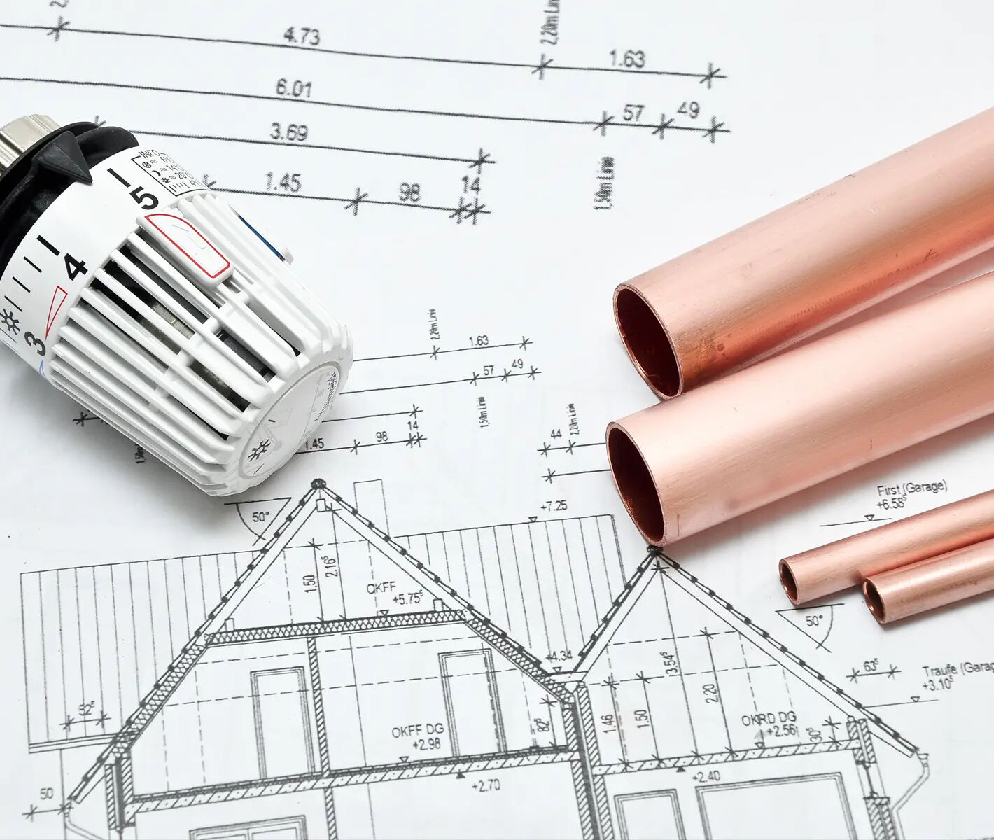 Ein Thermostat und Kupferrohre liegen auf einem Bauplan, der ein Haus zeigt. Der Bauplan enthält Maße und technische Zeichnungen, die Details der Konstruktion darstellen.
