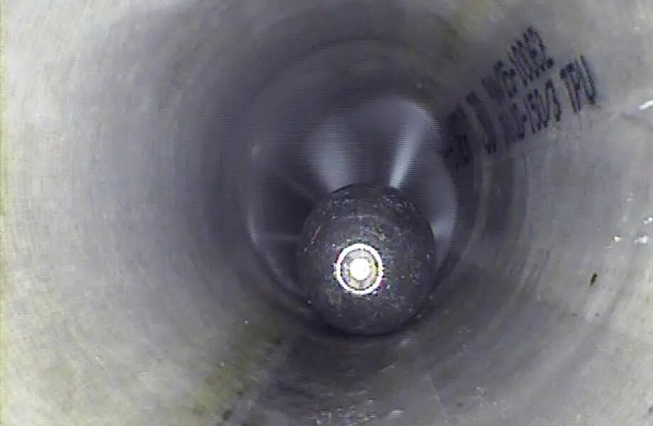 Blick in das Innere eines Rohres mit einer mechanischen Vorrichtung im Zentrum, die sich zu drehen scheint. Die Wände des Rohrs sind metallisch und sauber. Ein Teil der Rohrbeschriftung ist rechts zu erkennen.