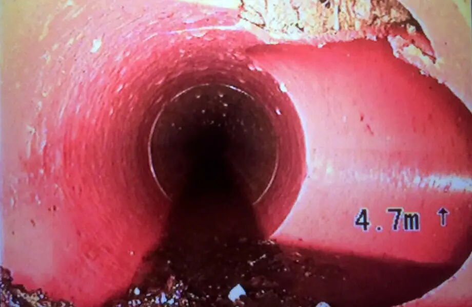 Blick in ein Rohr von innen, das eine gleichmäßige, rötliche Oberfläche hat. Am Boden des Rohrs sind dunkle Ablagerungen zu sehen. Rechts unten ist die Angabe "4.7 m" zu erkennen.