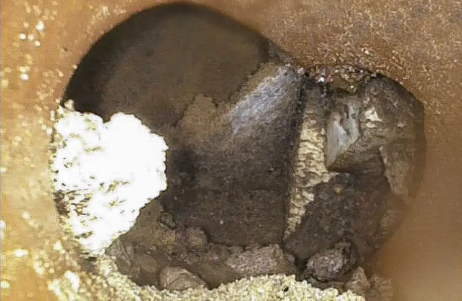 Ein rundes Loch in einem braunen Material, das möglicherweise Erde oder Stein ist. Der Boden des Lochs zeigt dunkle, unregelmäßige Flächen mit einer helleren, strukturierten Stelle links im Bild.